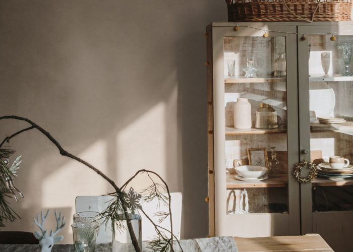 Elegant aesthetic home living or dinning room interior design with dinner table, linen table cloth, fir branch bouquet, Christmas wreath, neutral dusty pink walls. Sunlight shadows on the wall