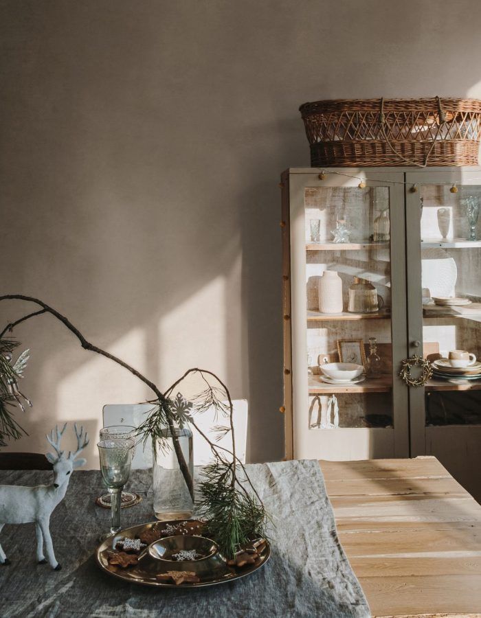 Elegant aesthetic home living or dinning room interior design with dinner table, linen table cloth, fir branch bouquet, Christmas wreath, neutral dusty pink walls. Sunlight shadows on the wall